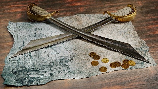 Dos sables cruzados sobre una pergamino en el que hay dibujado un barco. Tambien se ven unas cuantas monedas doradas