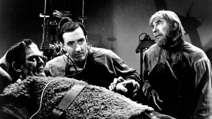Escena en blanco y negro donde se ve al monstruo en una camilla, al doctor Frankenstein auscultándole y al ayudane Igor junto a ellos